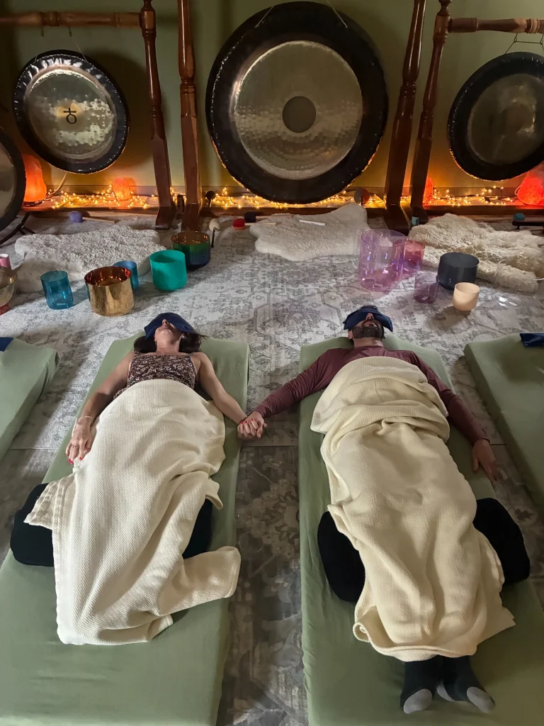 Couple resting on cushioned sound healing beds at Sedona Crystal Temple with crystal singing bowls and large gongs