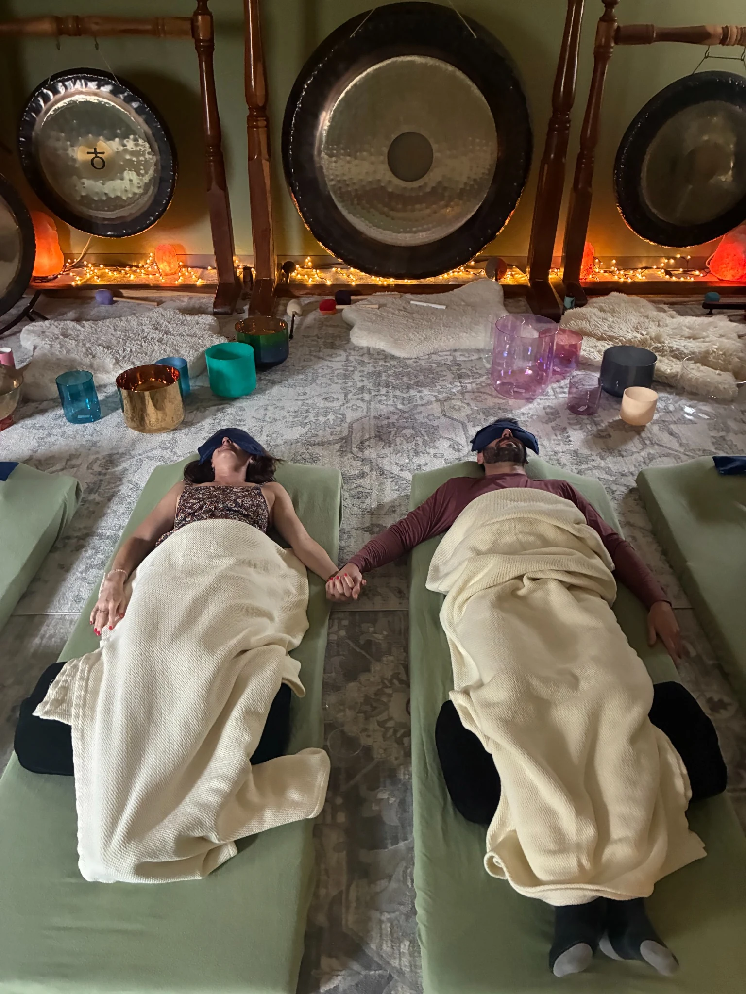 Couple resting on cushioned sound healing beds at Sedona Crystal Temple with crystal singing bowls and large gongs